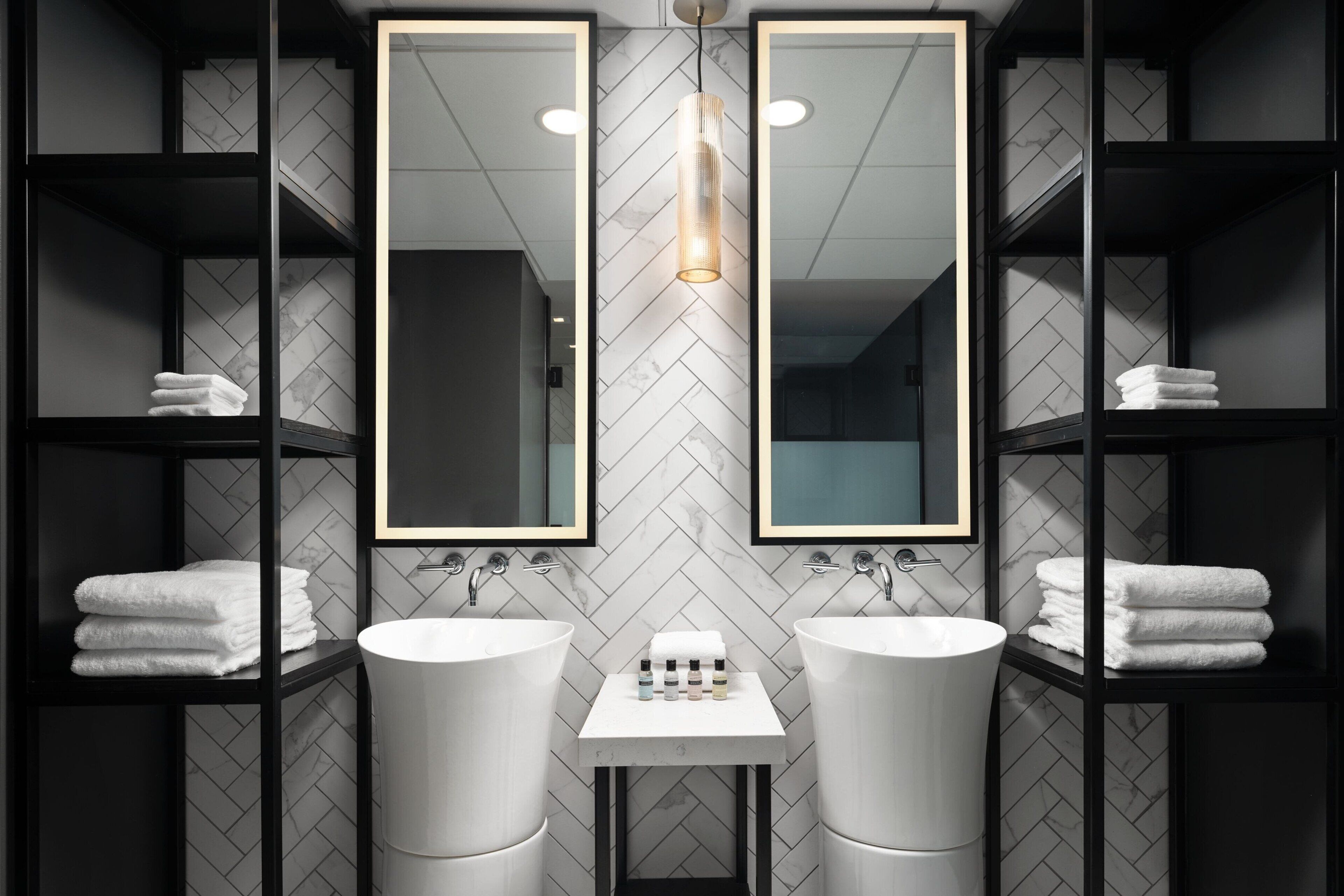 A modern bathroom with two sinks, mirrored cabinets, and a central shelf with toiletries.