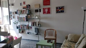 Una sala de estar con un sofá, una silla, una mesita y una estantería llena de libros y objetos decorativos.
