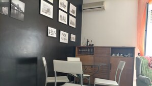 Una habitación con una pared oscura, piso de baldosas, una silla blanca, una mesa de vidrio y un armario con vajilla.