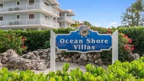 Placa para Ocean Shore Villas, com um edifício de vários andares ao fundo.