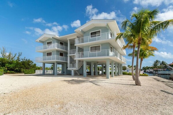 A multi-story beachfront property with balconies, a covered patio, and a palm tree.