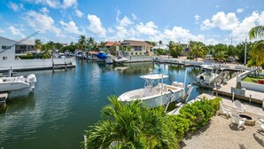 Uma marina com barcos atracados, uma pequena área de estar à beira da doca e um edifício ao fundo.