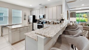 A modern kitchen with a large island, stainless steel appliances, and a dining area with bar stools. - 6 Bedrooms/ 6.5 Bathrooms/ Encore (7514 MA) (Kissimmee)