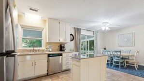 A kitchen with a dishwasher, a coffee maker, and a window with curtains. - Two Tides | Two Units in One | Screened In Porch | Steps to the Beach! (Folly Beach)