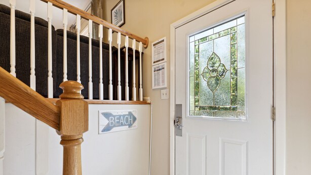 A staircase with a wooden handrail leading to a door with a glass panel. A sign on the wall reads "BEACH". - Two Tides | Two Units in One | Screened In Porch | Steps to the Beach! (Folly Beach)