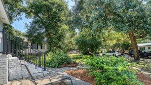 A paved outdoor area with steps leading up to a building, surrounded by greenery and trees. - Two Tides | Two Units in One | Screened In Porch | Steps to the Beach! (Folly Beach)