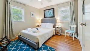 A neatly arranged bedroom with a bed, bedside tables, a chair, and a ceiling fan. - Two Tides | Two Units in One | Screened In Porch | Steps to the Beach! (Folly Beach)
