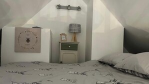 A bedroom with a sloped ceiling, a bed with a floral-patterned bedspread, a bedside table with a lamp, and a framed picture on the wall. - Claymires Bothy Cottage Nr Loch Lomond & Stirling (Stirling)