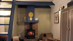 A cozy living room with a brick fireplace, a clock, and a plaid sofa. - Claymires Bothy Cottage Nr Loch Lomond & Stirling (Stirling)