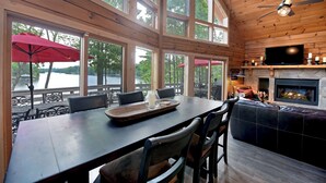 Un intérieur en bois comprenant une table à manger, des chaises, une cheminée et de grandes fenêtres donnant sur un lac.