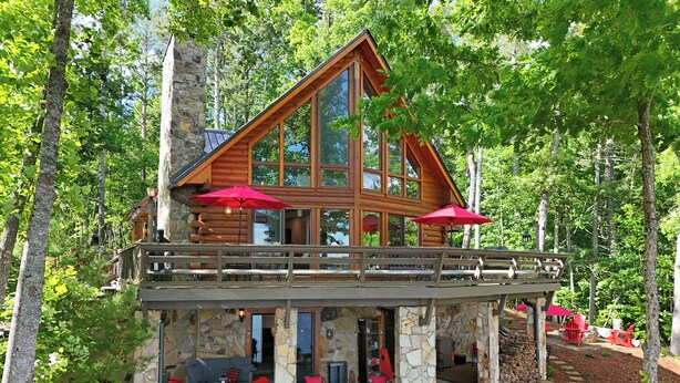Une cabane en rondins avec des fondations en pierre, un balcon et des parasols rouges.