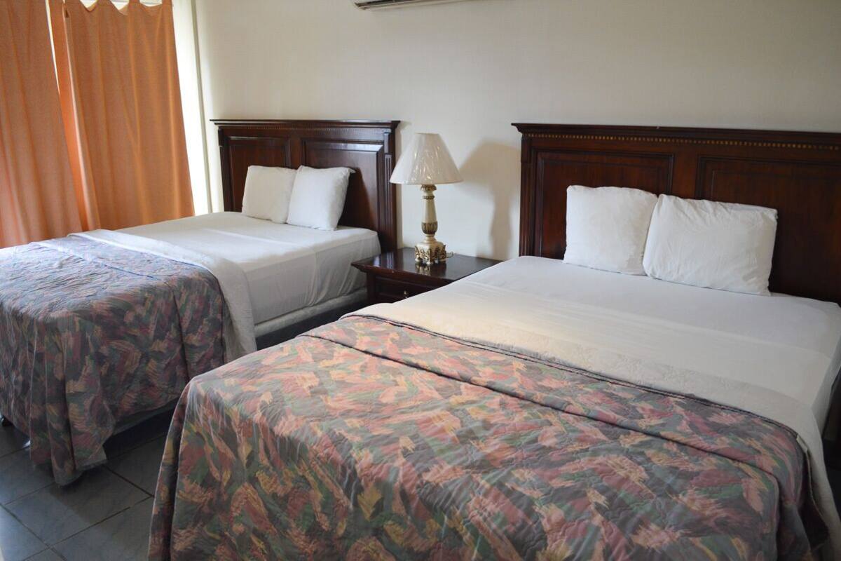 Une chambre d’hôtel avec deux lits, chacun doté d’une tête de lit en bois et de linge de lit blanc. Une table de chevet avec une lampe se trouve entre les deux lits.