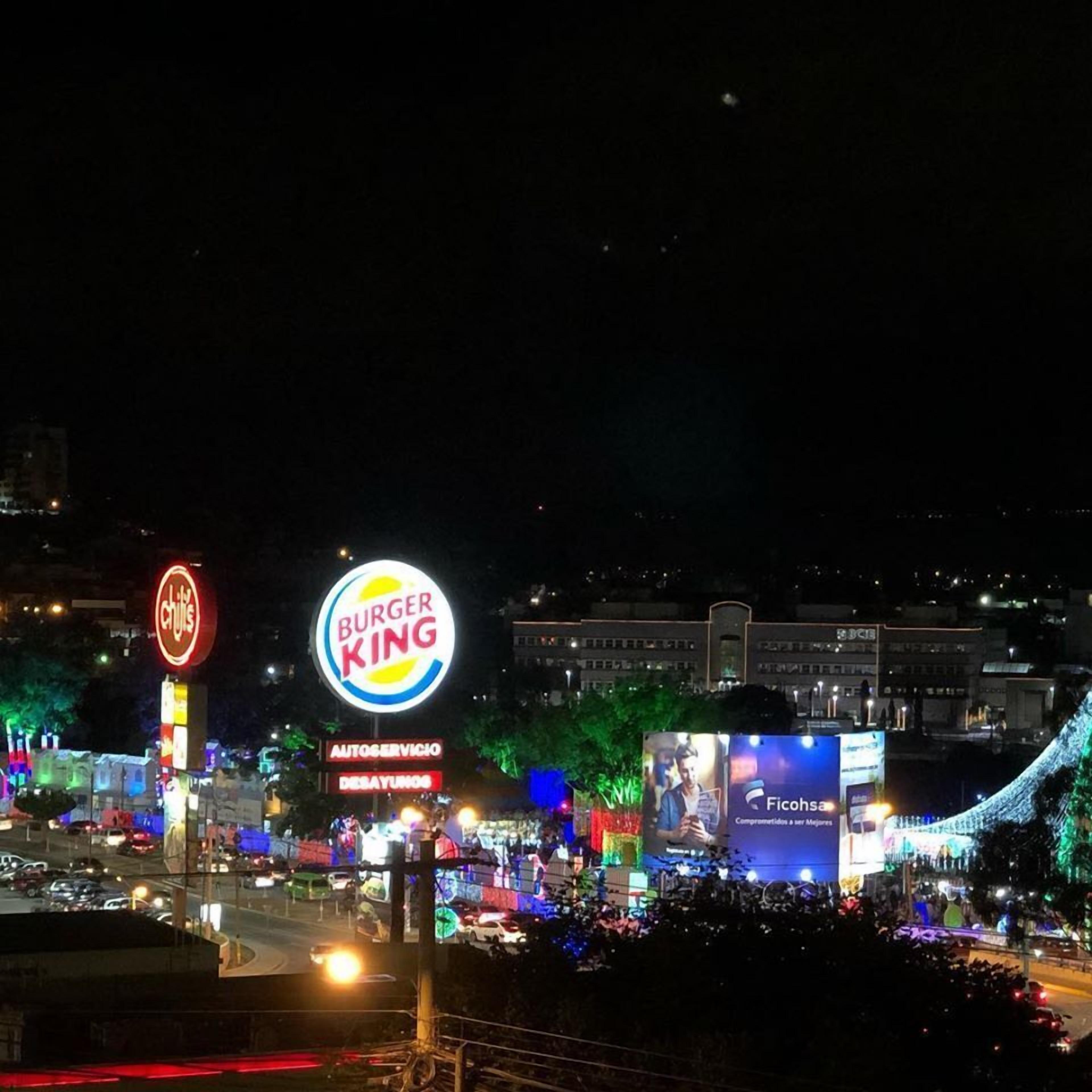 Un cartello Burger King con un grande logo illuminato, un cartello Chili's e una pubblicità di Ficoha.