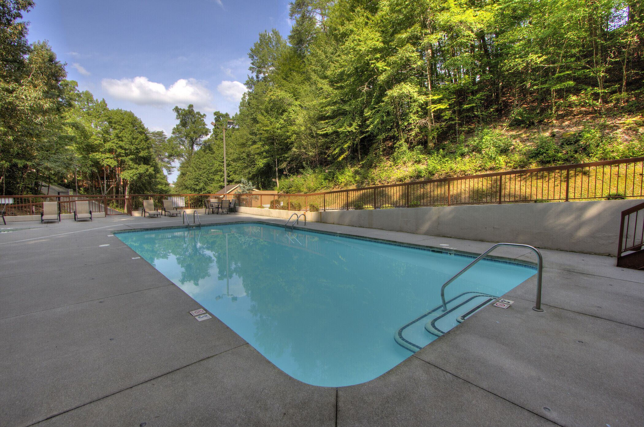 Une piscine rectangulaire avec un escalier en métal, entourée d’une terrasse en béton et d’une clôture en bois.