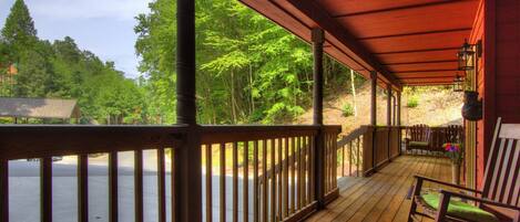 A wooden deck with a view of a forest and a lake.