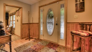 Un foyer doté d’un plancher en bois, d’un tapis à motifs, d’un banc avec un coussin et d’une porte ornée de panneaux de vitrail.