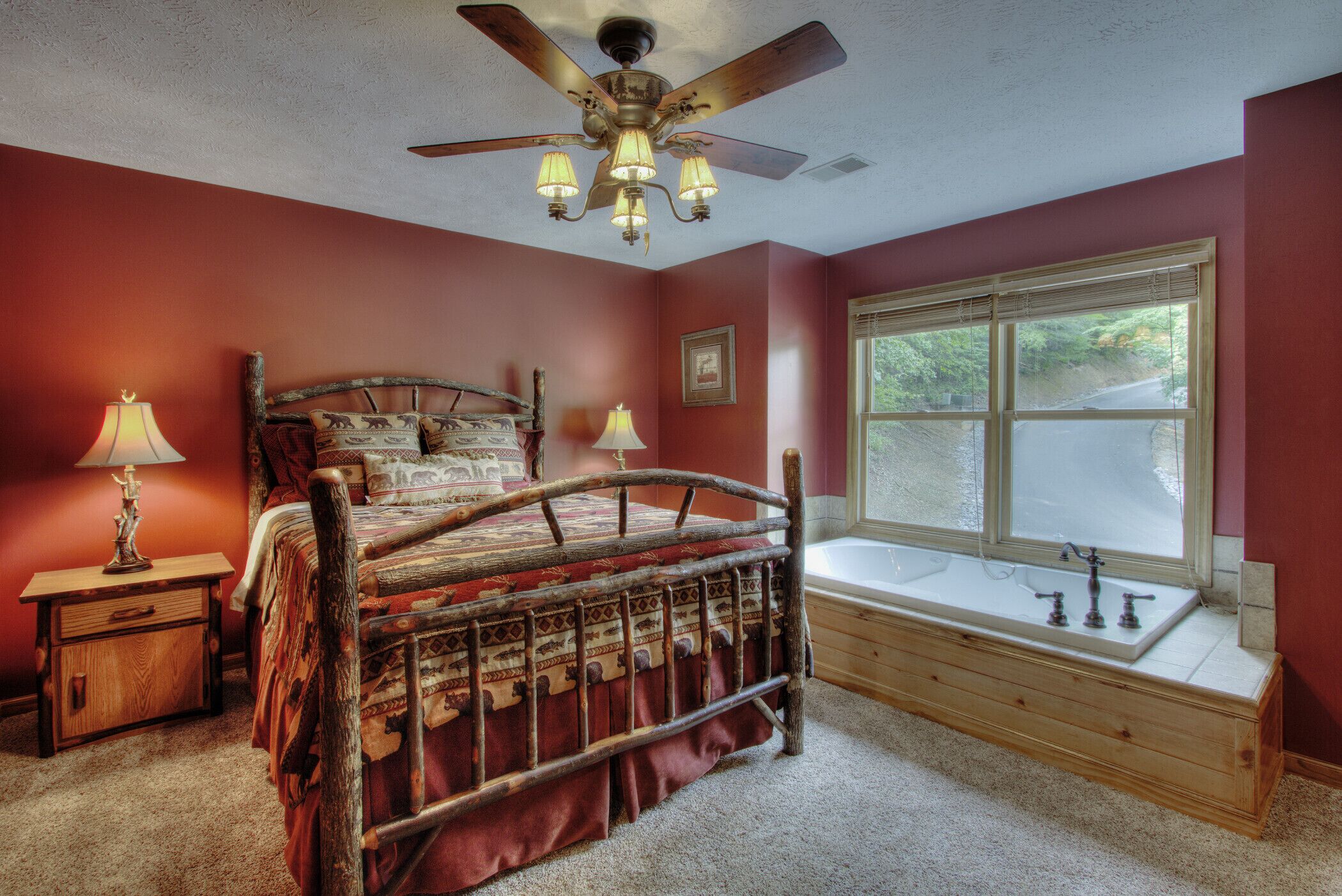 A bedroom with a wooden bed, a window with a view, a ceiling fan, and a nightstand with a lamp.