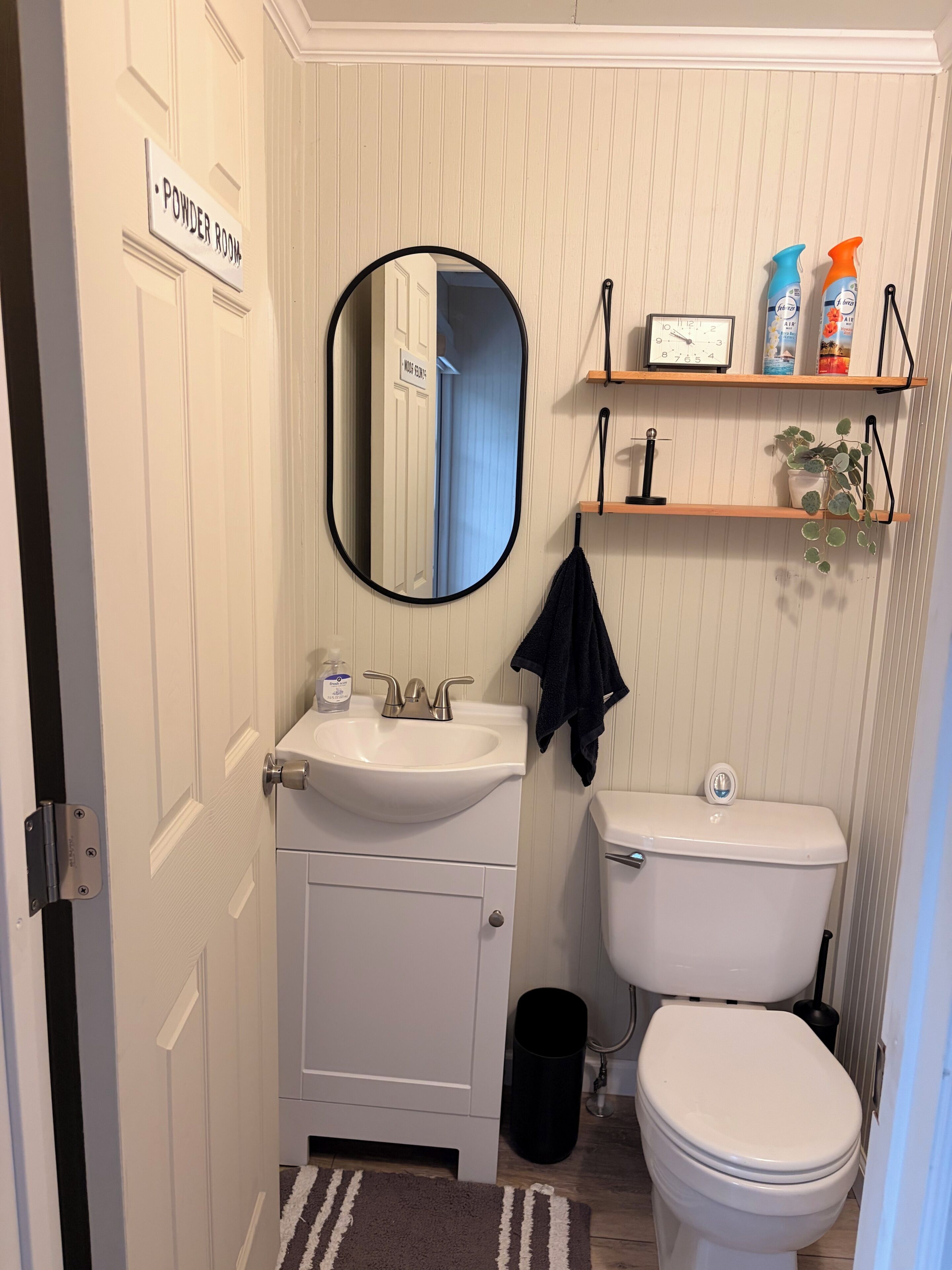 A bathroom with a sink, mirror, toilet, and shelves with toiletries.