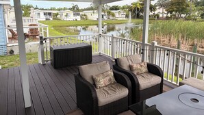 A covered outdoor deck with wicker furniture, a view of a pond, and a row of houses in the background. - Newly renovated, large deck, backs onto large pond (Sarasota)