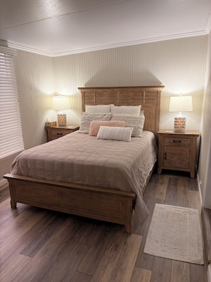 Een slaapkamer met een houten bed, twee nachtkastjes, een bedlampje en een vloerkleed.