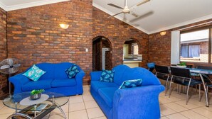 A room with two blue sofas, a glass coffee table, a fan, and a dining area with chairs and a table. - Boasting some of Bribie's Best Waterviews (BONGAREE)