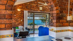 A kitchen with a brick wall, a dining area with a table and chairs, and a view of the sea through a glass door. - Boasting some of Bribie's Best Waterviews (BONGAREE)