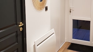 Un pasillo con una puerta negra, un radiador blanco, un espejo decorativo y una ventana con vistas azules.