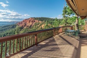A wooden deck with a railing overlooking a forested valley and a mountain.