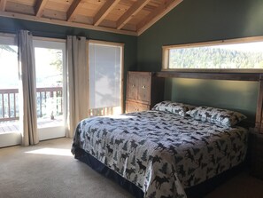 Un dormitorio con cama, ventana que ofrece vistas a árboles y techo de madera.