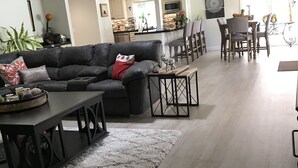 A modern living room with a grey sofa, a coffee table, and a dining area with chairs and a table.