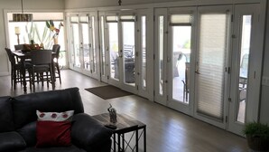 A spacious living room with a black leather sofa, a dining table with chairs, and a large window with a view of the outdoors.