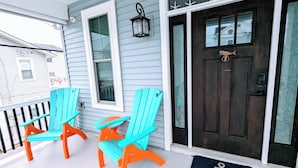 A porch with two turquoise Adirondack chairs, a dark wooden door, and a small outdoor light fixture. - 4 BR/ 4 BA/ Single Family - 2 Primary Suites (Ocean City)