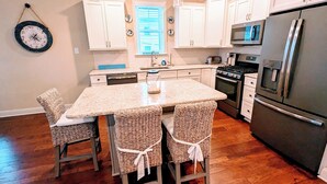 A kitchen with white cabinets, a central island with chairs, a refrigerator, and a microwave. - 4 BR/ 4 BA/ Single Family - 2 Primary Suites (Ocean City)