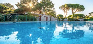 Une piscine aux eaux cristallines, dotée d’un escalier, entourée d’arbres et bordée d’un bâtiment en pierre.