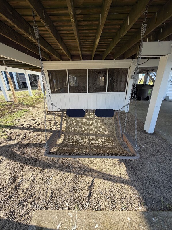A covered outdoor swing area with a wooden swing set, chain links, and a metal frame. - Cozy beach house with newly renovated kitchen-just a 1 minute walk to the beach (Rodanthe)