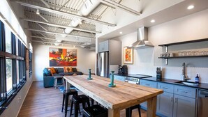 Een moderne keuken met een lange houten tafel, barstoelen, een koelkast en een koffieapparaat.
