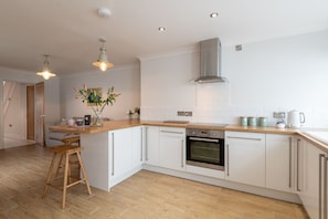 A modern kitchen with white cabinets, a wooden countertop, a stainless steel oven, and a hanging light fixture.