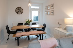 A dining area with a wooden table, black chairs, a bench, a wall clock, framed pictures, a lamp, and a bird sculpture.