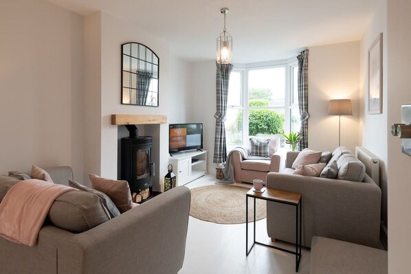 A modern living room with a fireplace, sofa, television, and a view of greenery outside.