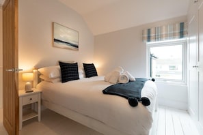 A bedroom with a bed, bedside table, lamp, window, and artwork.