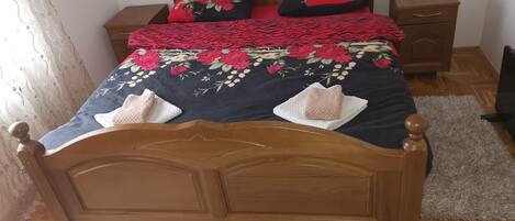 A neatly made bed with a floral bedspread, two pillows, and a bedside table with a lamp.