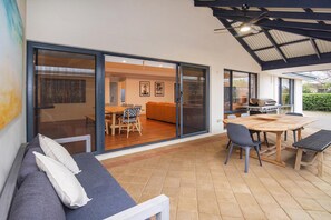 A modern patio with a wooden table and chairs, a sofa, and a sliding glass door leading to an interior dining area. - House 02 - The Dunsborough Retreat (Dunsborough)