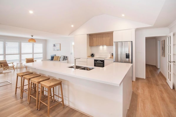 A modern kitchen with a large island, wooden stools, and a dining area with a table and chairs.