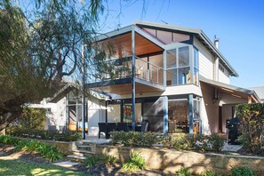 A modern two-story house with a balcony, outdoor seating, and a well-maintained garden.