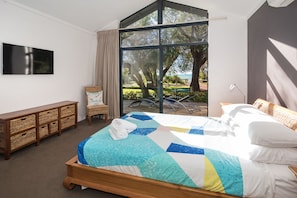 A bedroom with a large bed, a TV, a wicker chair, and a view of the outdoors.