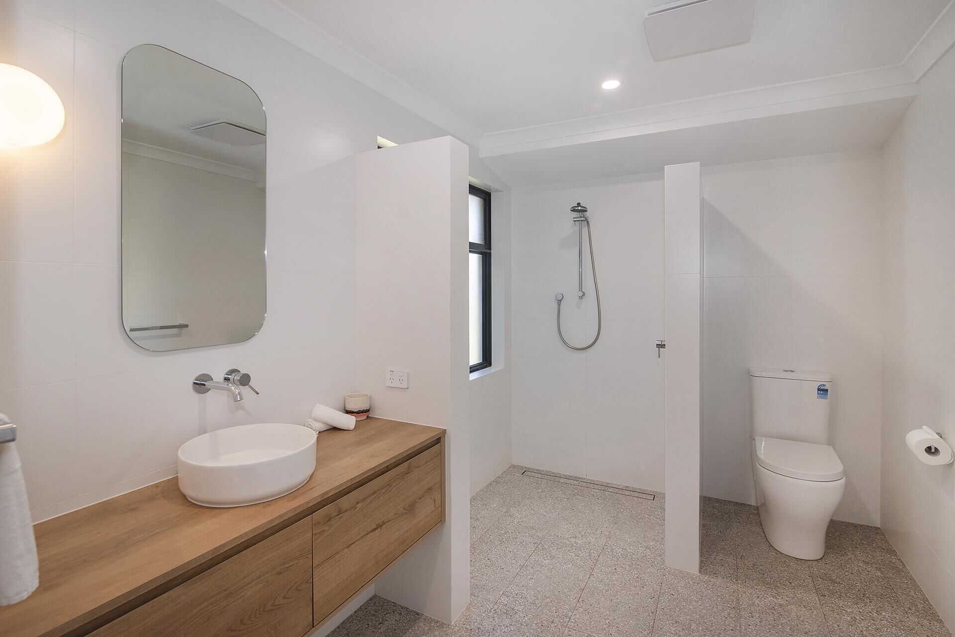 Une salle de bain moderne avec un meuble-lavabo en bois, un lavabo rond, des toilettes et une douche.