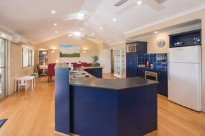 A spacious kitchen with a central island, a dining area with red chairs, and a view of the outdoors. - House 20 - The Garden House Dunsborough (Dunsborough)
