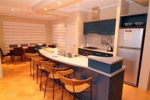 A modern kitchen with a central island, bar stools, a stove, and a refrigerator. - House 16 - Jewel of the Bay Dunsborough (Dunsborough)