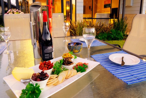 A table set for a meal with a bottle of wine, glasses, and a variety of appetizers. - House 16 - Jewel of the Bay Dunsborough (Dunsborough)