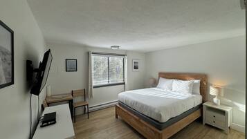 A bedroom with a bed, bedside tables, a desk, and a window with blinds.